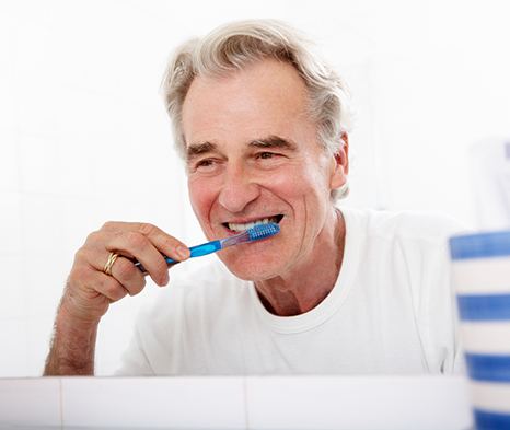 Man smiling while brushing teeth in bathroom