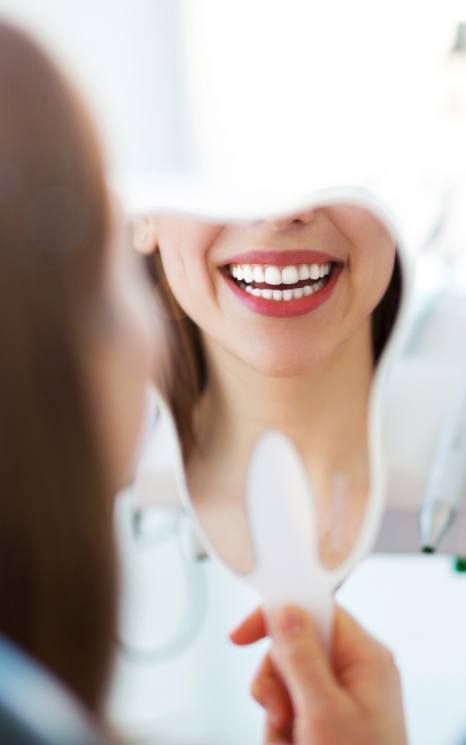 Woman looking at smile in mirror after cosmetic dental bonding