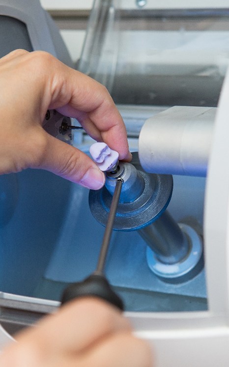 Technician taking dental crown out of milling machine