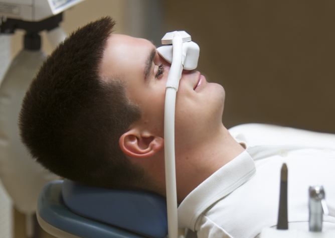 Man relaxing in dental chair with eyes closed and sedation dentistry mask over his nose