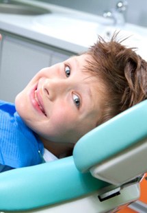 young boy giving thumbs up while sitting in dental chair 