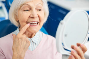 a woman pointing to a loose dental implant while sitting in a treatment chair